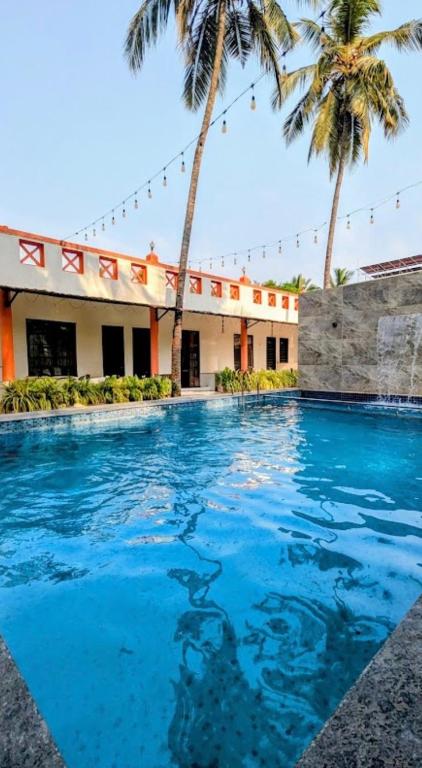 a swimming pool in front of a building with palm trees at Second Home Stays at Arnav Cottages Alibag in Alibaug