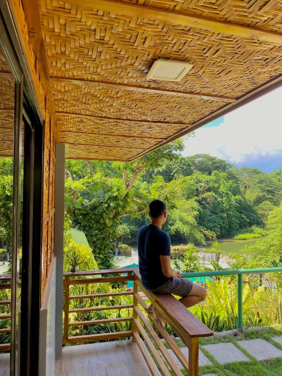 a man sitting on a porch looking out at the forest at Busai Dream Falls Resort in Loboc