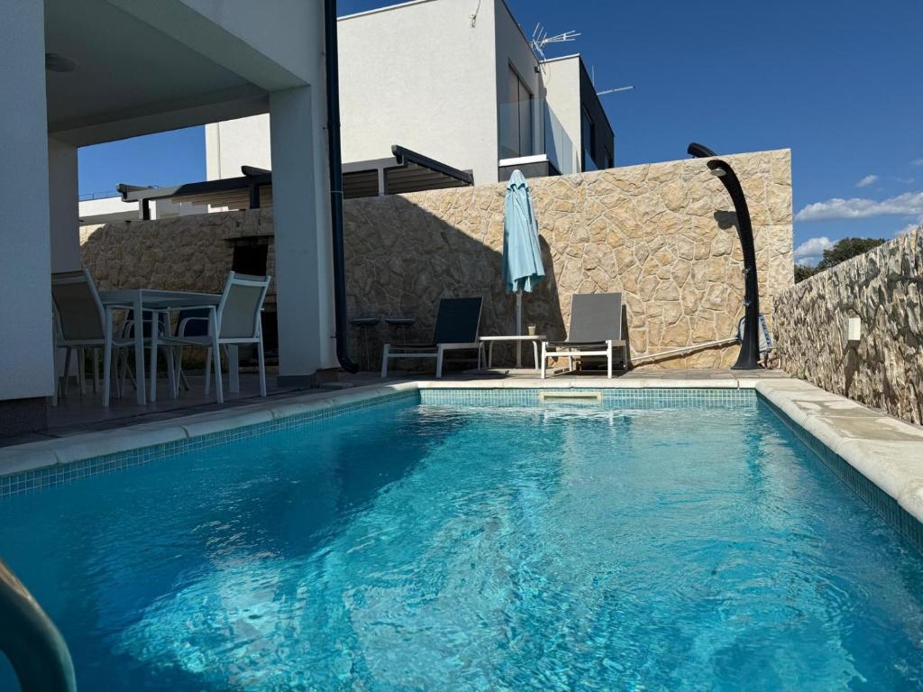 a swimming pool with a table and chairs next to a building at PALMandre (Pag Apartment Luxurious) in Mandre