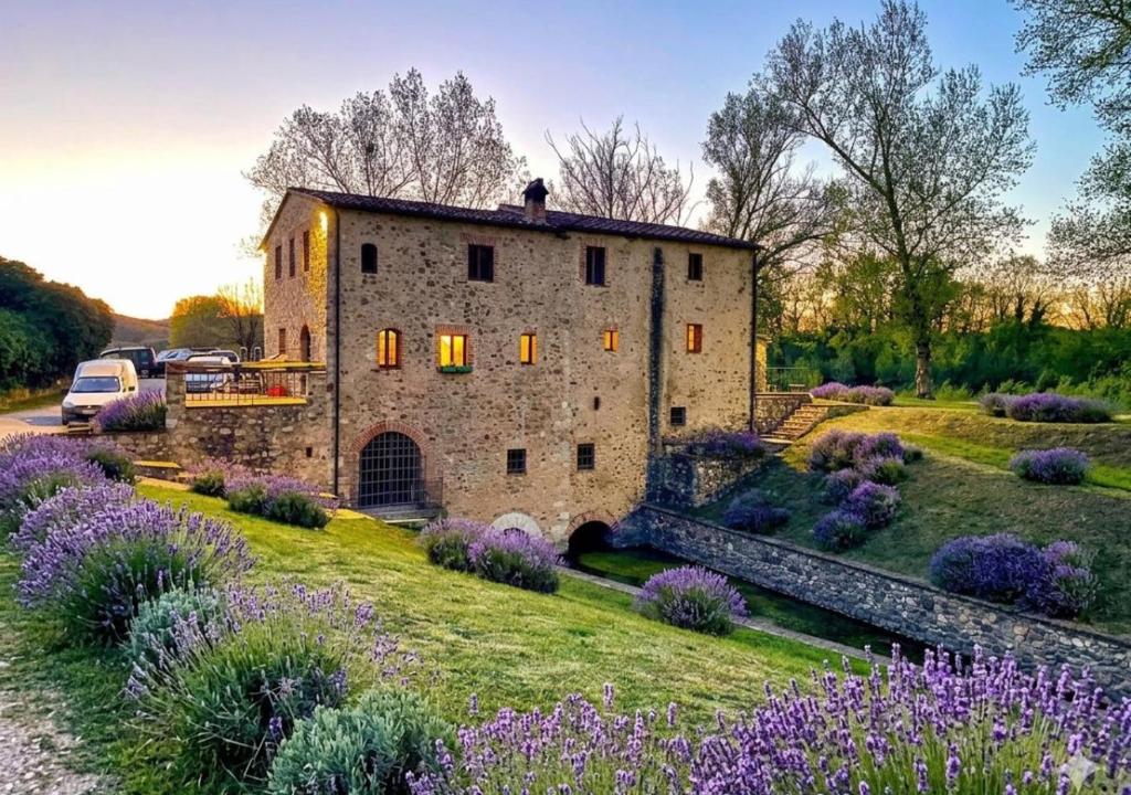 a large stone building with purple flowers in front of it at Mulino di Pari - Where Time Slows in Pari