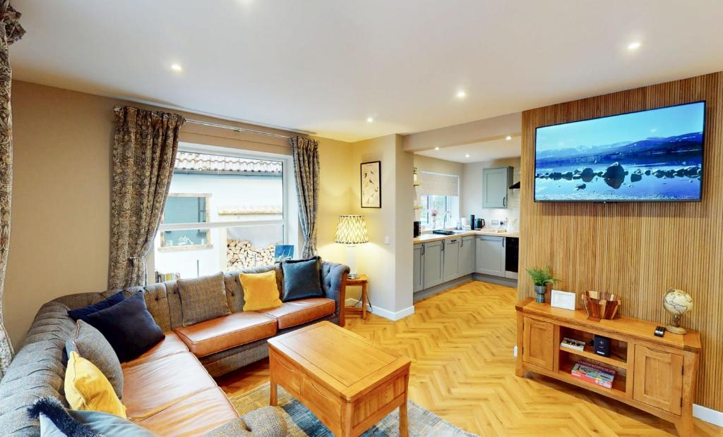 a living room with a couch and a television on a wall at Kestrel Lodge - hot tub , sauna, EV and bike storage in Aviemore