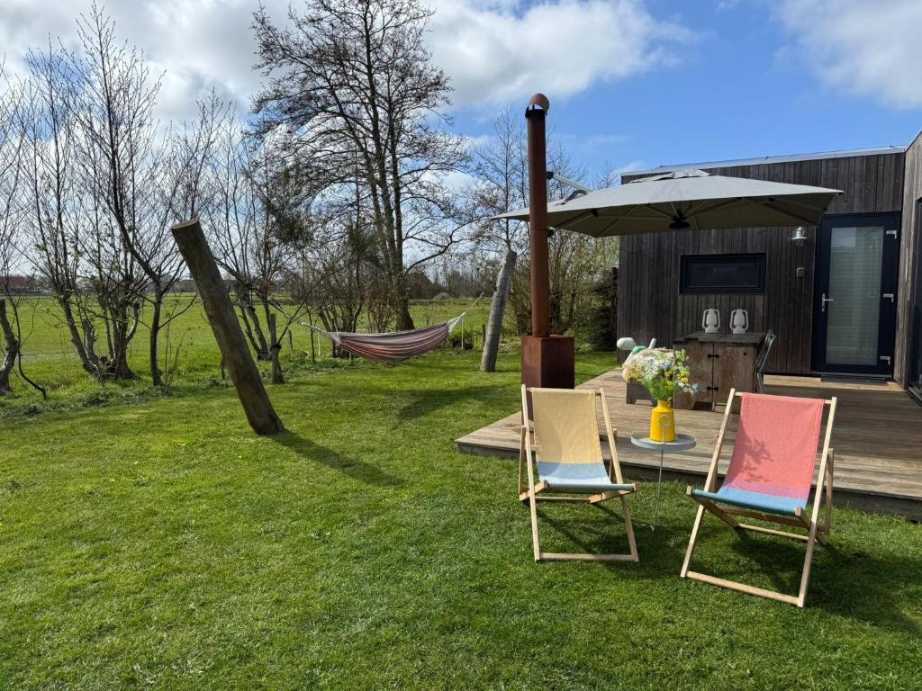 two chairs and a table with an umbrella in a yard at Sinne - Ecohuisjes Terschelling in Midsland