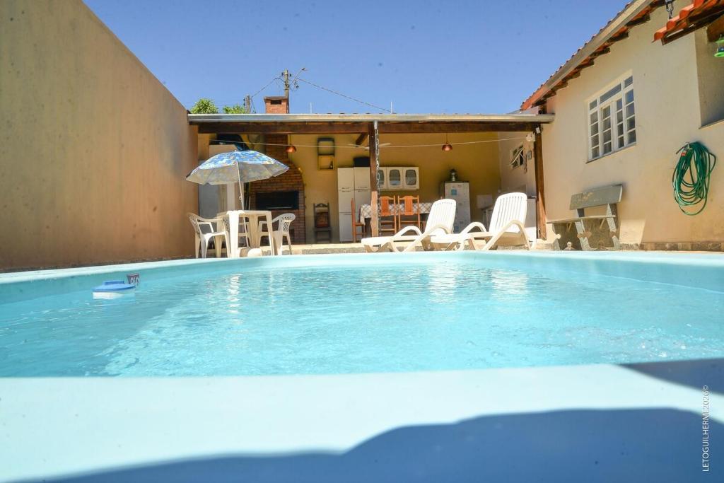 a large swimming pool with chairs and an umbrella at Casa Completa em Socorro SP - Com Piscina, Churrasqueira e Roupa de Cama in Socorro