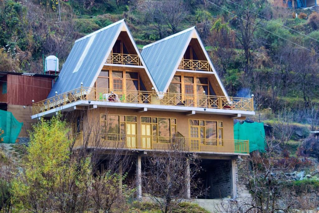 a large house with a blue roof on a hill at Clifton Chapter Cottage Tirthan in Banjār