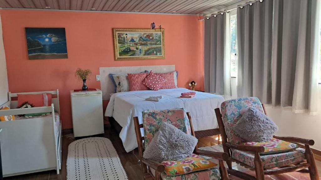 a bedroom with orange walls and a bed with chairs at Pousada Aconchego dos Puris in Resende