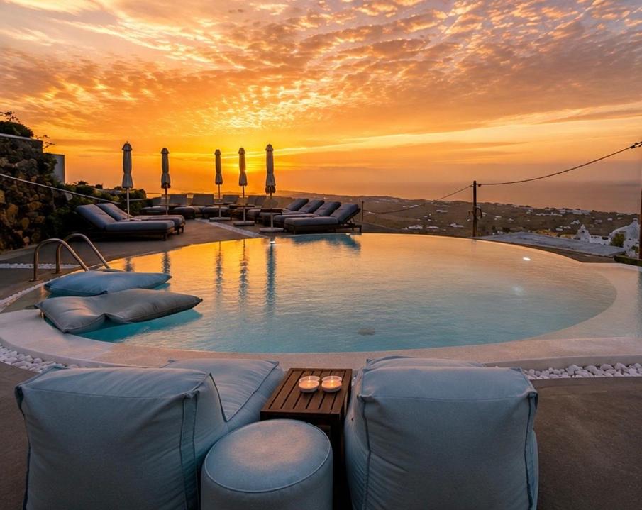 ein großer Swimmingpool mit Liegestühlen und ein Sonnenuntergang in der Unterkunft Aperanto Suites in Oia