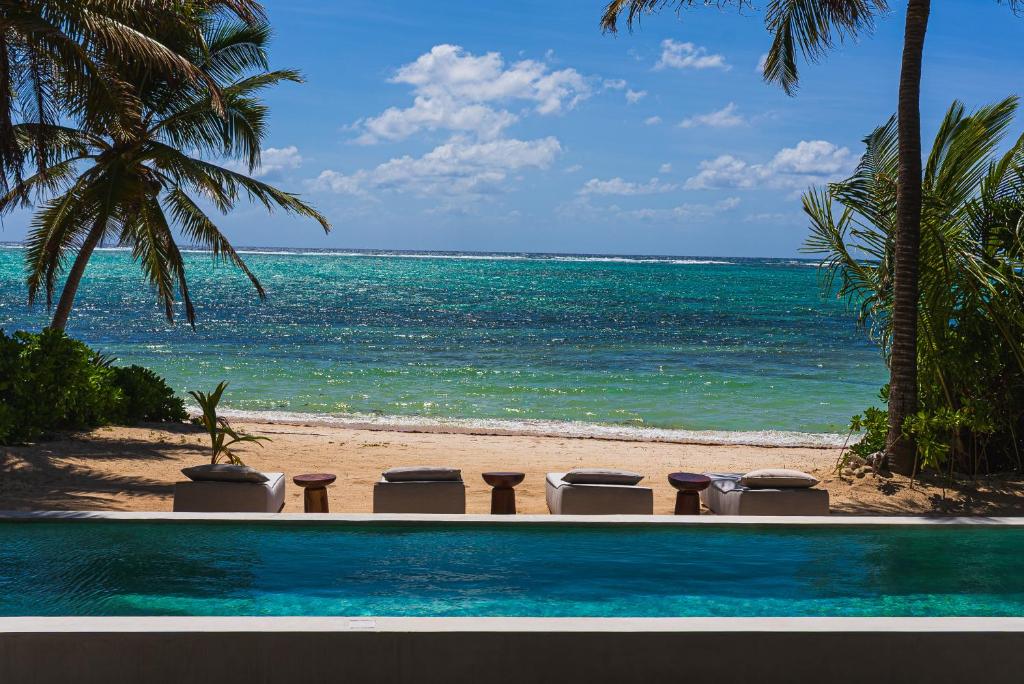 a pool with chairs on the beach next to the ocean at Luxury Beachfront 3BR Appartment in Tulum