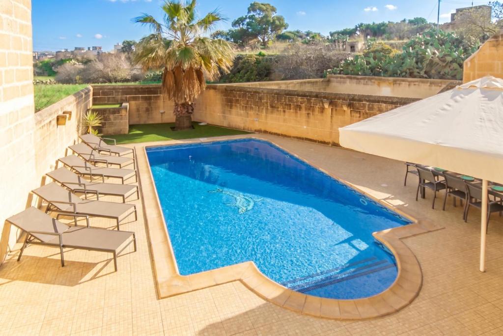 a swimming pool with chairs and a white umbrella at Centre Island Gozitan Farmhouse & Pool - Happy Rentals in Kerċem