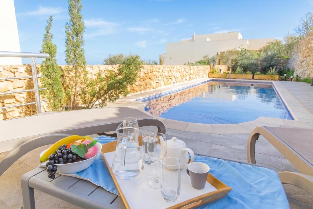 a table with wine glasses and a bowl of fruit next to a pool at Ta'Siku Gozitan villa Pool & hot tub - Happy Rentals in Il-Pergla