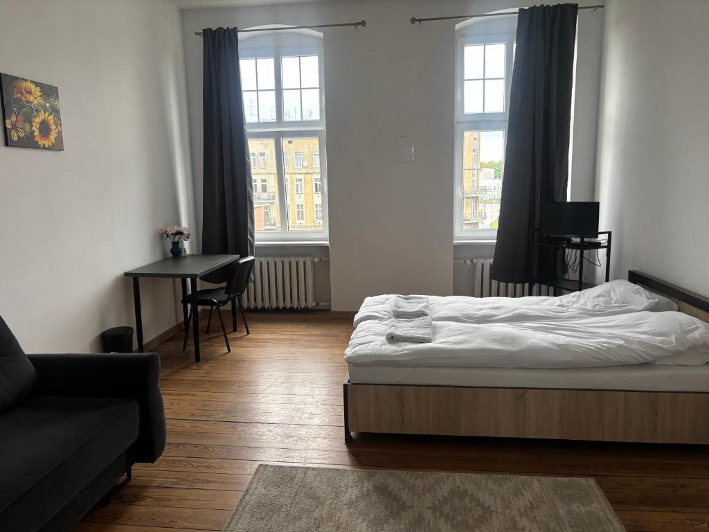 a bedroom with a bed and a table and two windows at Pokoje Zwycięstwa in Gliwice
