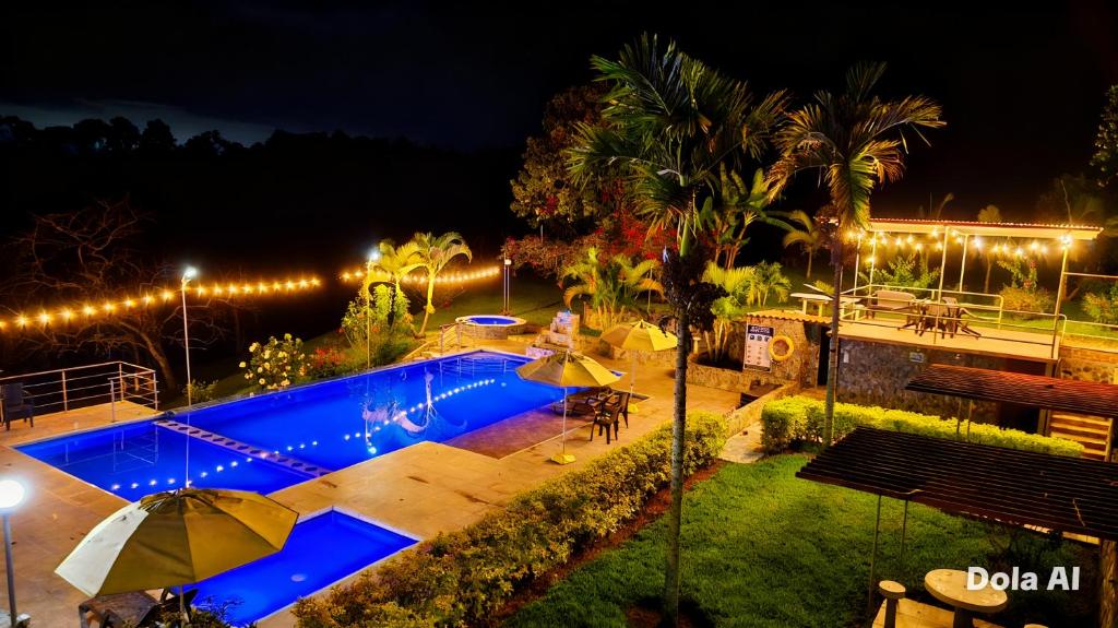 a swimming pool at night with umbrellas and a pool at Hotel Campestre Los Mangos in Quimbaya
