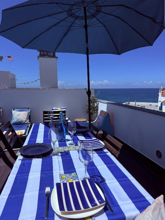 a table with a blue and white table cloth and an umbrella at Sunset Beach House in Zambujeira do Mar