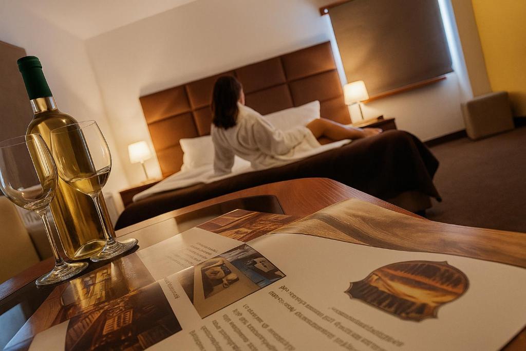 a woman sitting on a bed in a hotel room with a bottle of wine at Apartamenty Maciejowy Sad in Sady Dolne