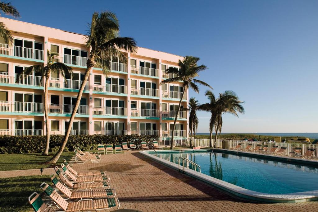 a large hotel with a swimming pool and palm trees at Sea Gardens Resort Studio Suite in Pompano Beach
