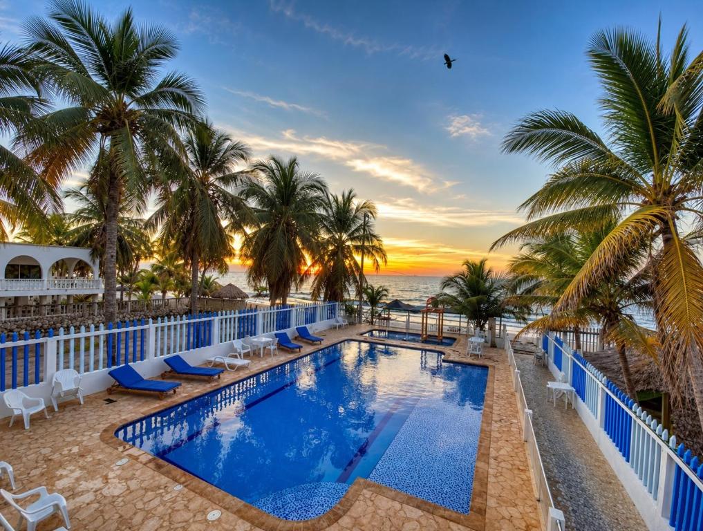 a resort pool with palm trees and the ocean at Hotel Playarena in Coveñas