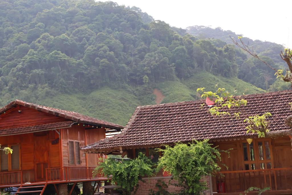 two wooden houses with a mountain in the background at ANOR Farmstay - Two Double Bed in Hue