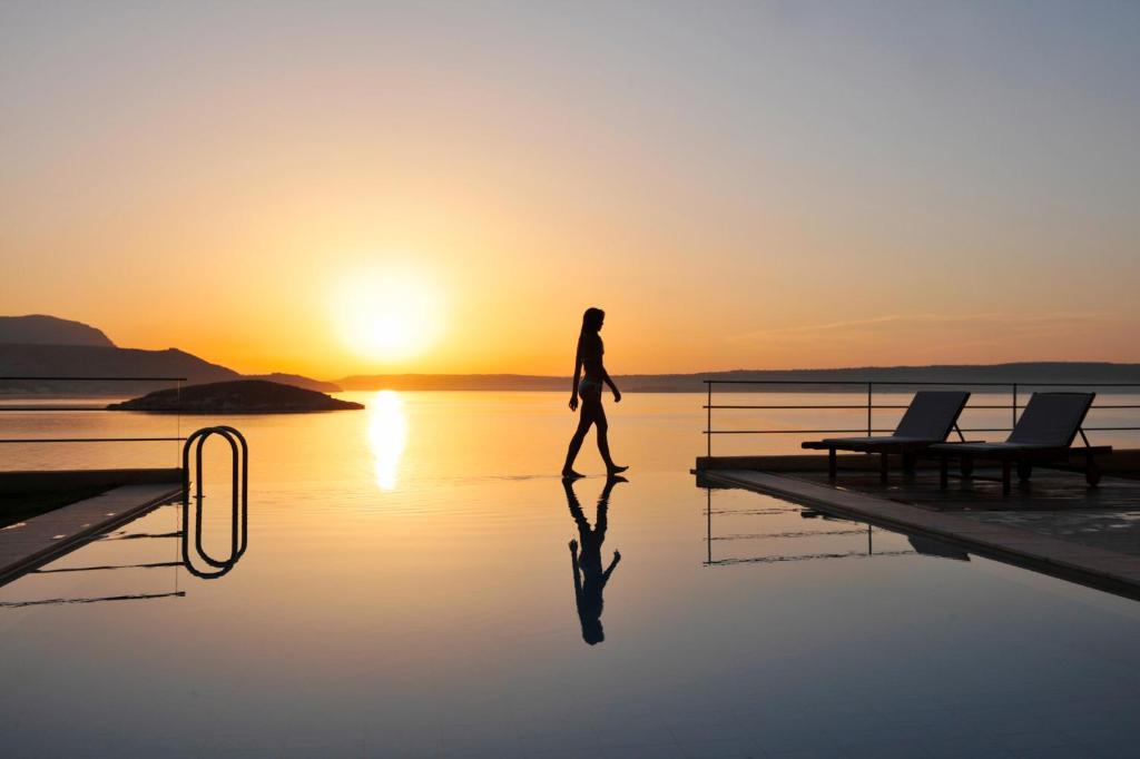 una persona caminando sobre el agua con la puesta de sol en el fondo en SK Place Luxury Seafront Villas Chania, en Almyrida