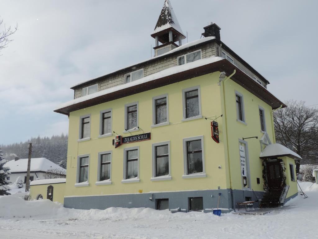a yellow building with a tower on top in the snow at Pension zur alten Schule in Bärenstein
