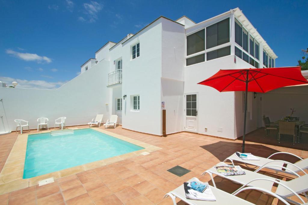 a villa with a swimming pool and a red umbrella at Villa Webb in Puerto del Carmen