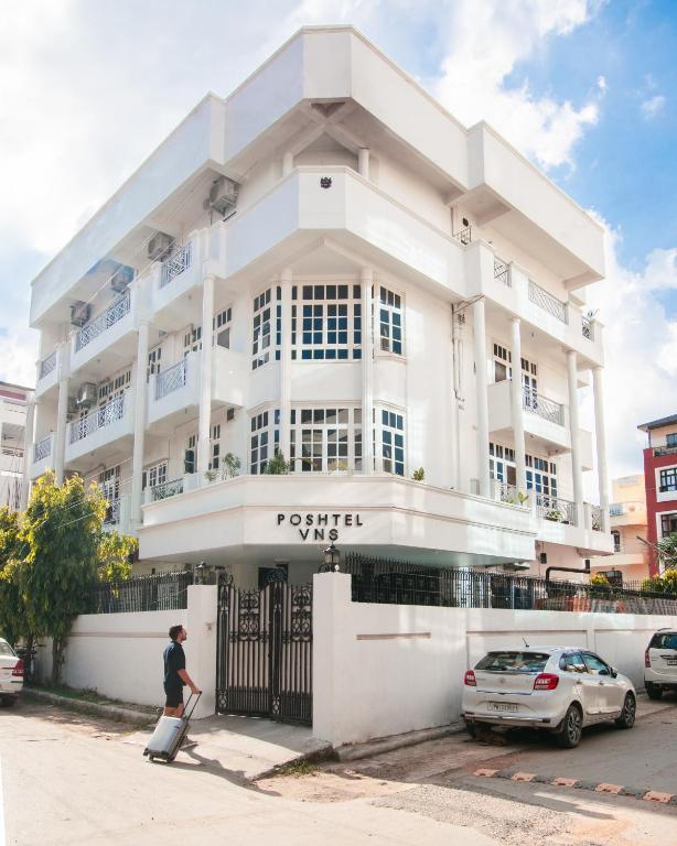 a woman walking in front of a white building at Poshtel VNS in Varanasi