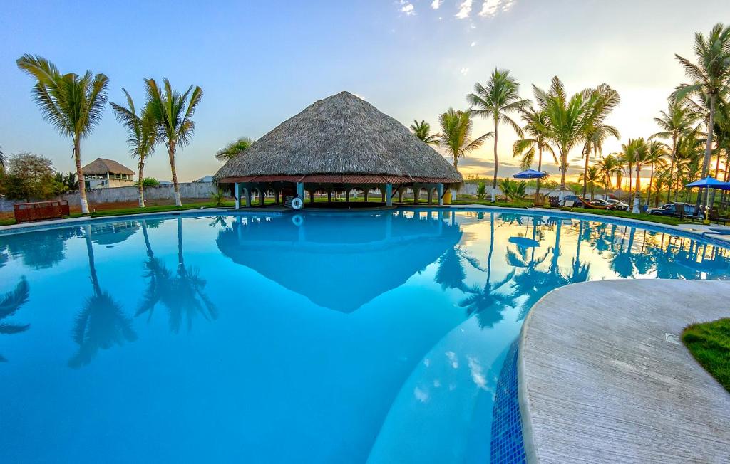 una gran piscina con un edificio con techo de paja y palmeras en Hotel Cafe del Sol, en Monterrico