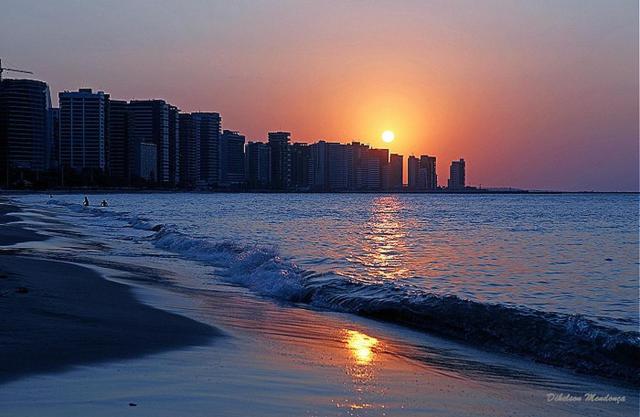 a beach with the sun setting over a city at Nalu Beach Hotel pousada in Fortaleza