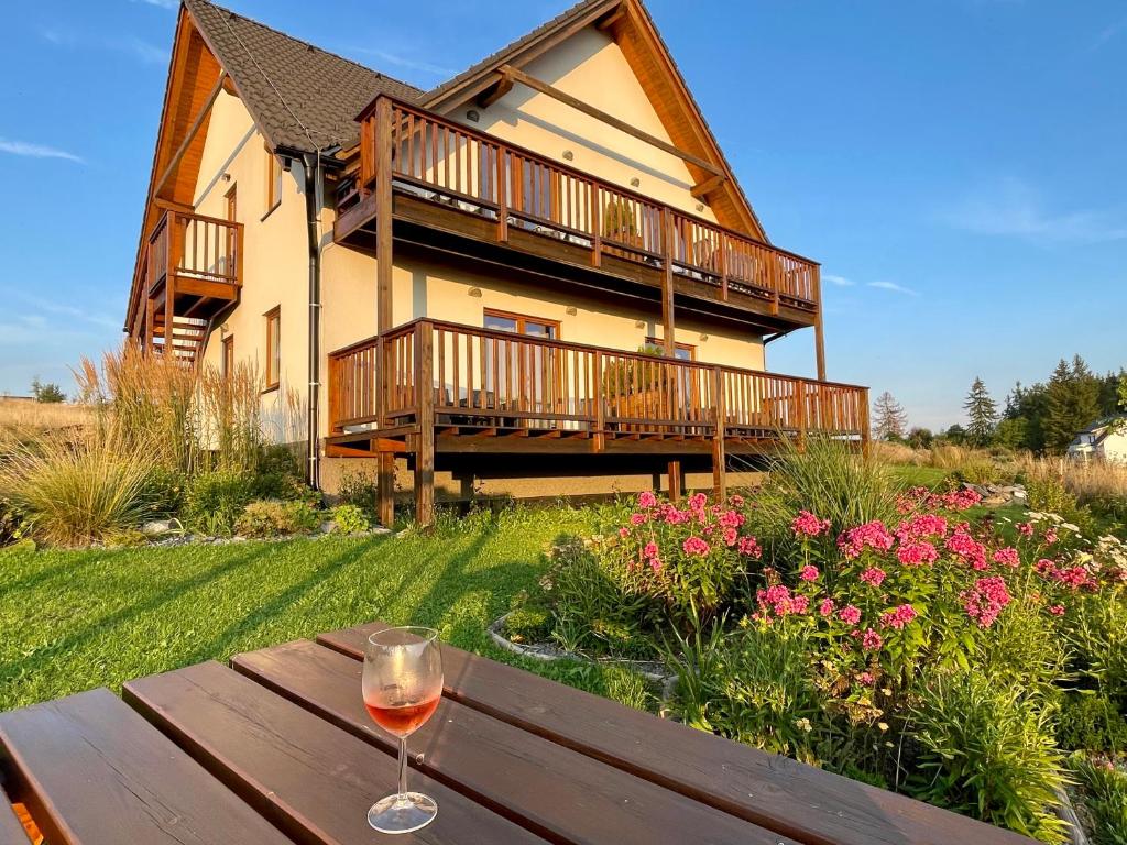 a glass of wine sitting on a wooden table in front of a house at Apartmány MAX - Jeseníky in Vaclavov u Bruntalu