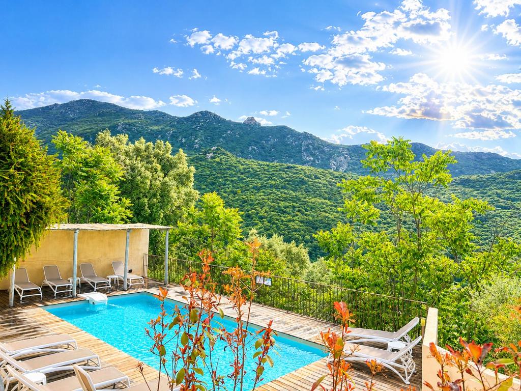 a villa with a swimming pool and mountains in the background at Hôtel Villa Les Orangers in Olmeto