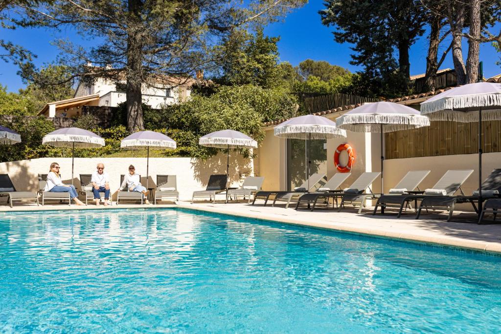 a pool with people sitting on chairs and umbrellas at Hôtel La Garrigue & Bar Le Perchoir in Venasque