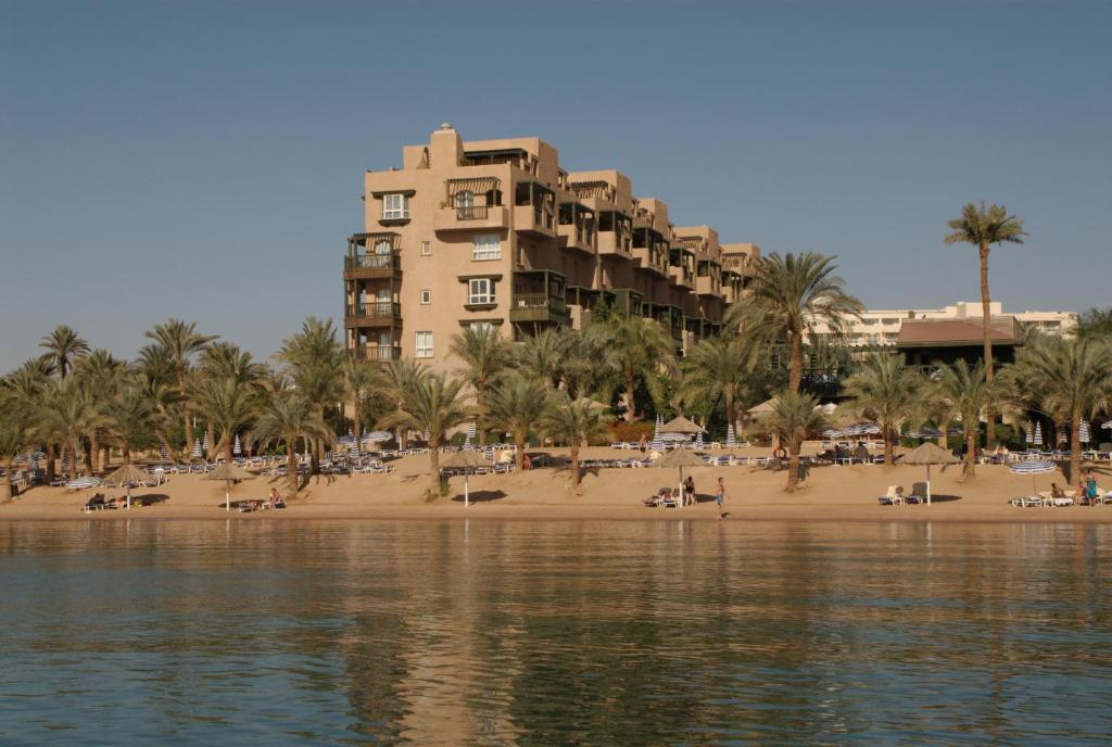 a hotel on a beach with palm trees and a building at Mövenpick Resort & Residences Aqaba in Aqaba
