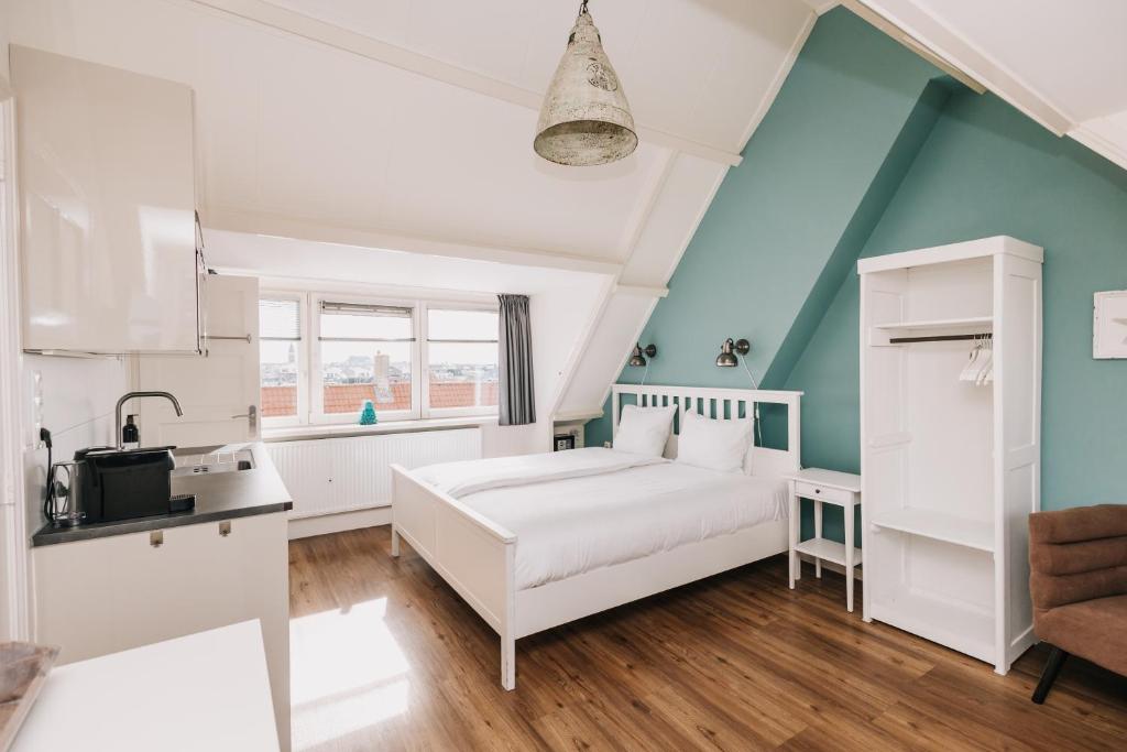 a bedroom with a white bed and a kitchen at Divi Divi Zandvoort in Zandvoort
