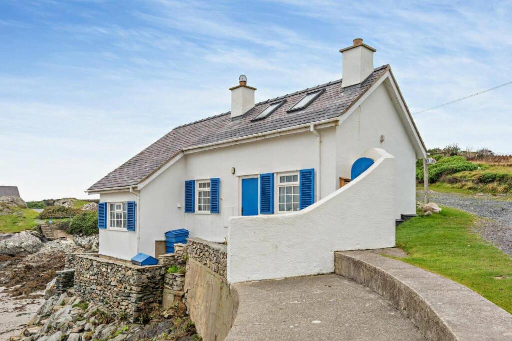 a white house with blue shutters and a staircase at Boatman's Cottage in Rhoscolyn