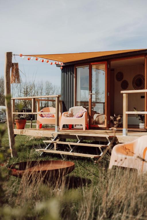 a small house with a porch and chairs in a field at Tiny Cabana in Scharendijke