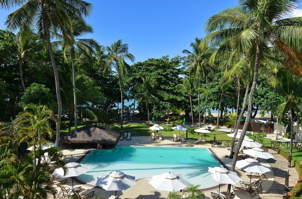 a swimming pool with umbrellas and tables and palm trees at Iara Beach Hotel Boutique in Salvador