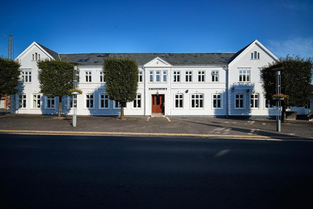 a large white building with a red door on a street at Westergaards Hotel in Videbæk