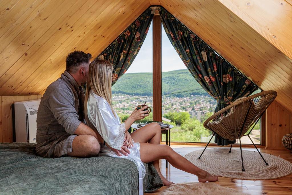 a man and woman sitting on a bed looking out a window at a Ficak in Miskolc
