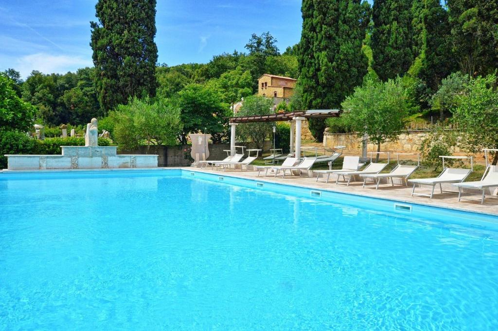 a large swimming pool with chairs and a fountain at Le Querciolaie with Geothermal Pool - by PosarelliVillas in Monteverdi Marittimo