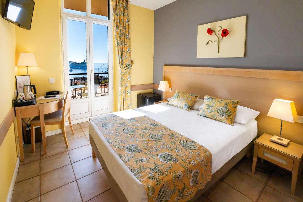 a hotel room with a bed and a desk and a window at Hôtel La Flore in Villefranche-sur-Mer