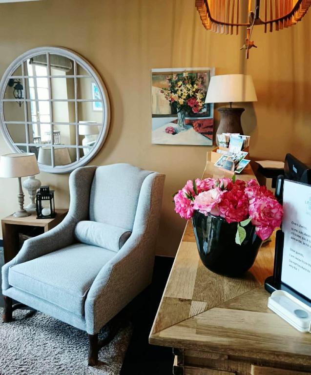 un salon avec un fauteuil et un vase de fleurs sur une table dans l'établissement Hôtel Traiteur Les Ormes, The Originals Relais, à Barneville-Carteret