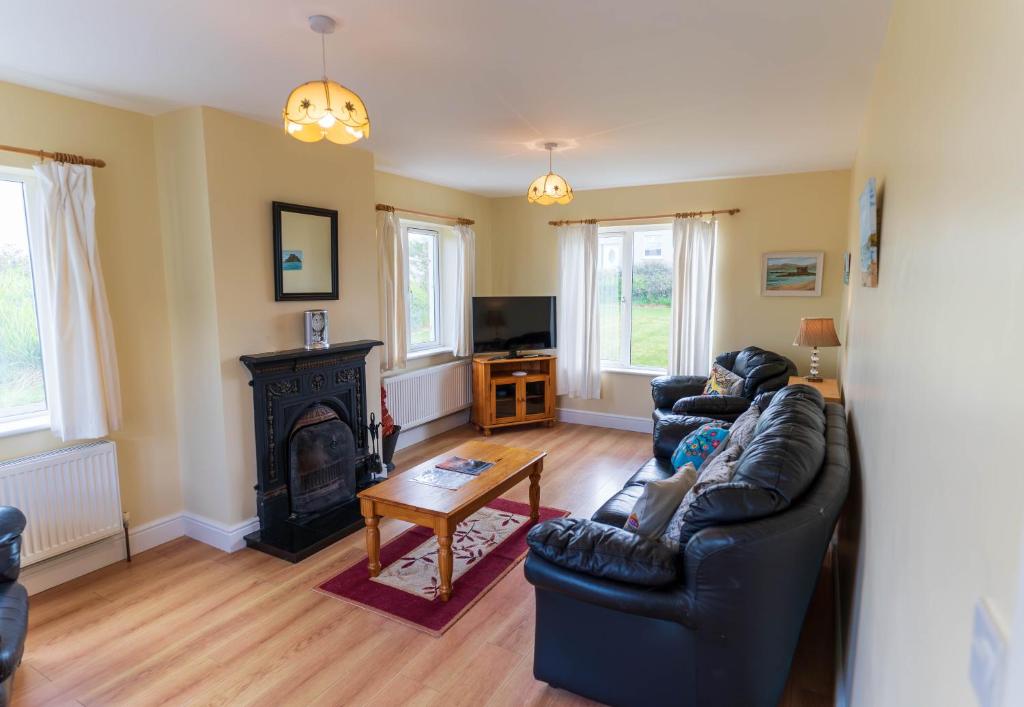 a living room with a black leather couch and a fireplace at Montbretia - Ballinskelligs in Dungeagan