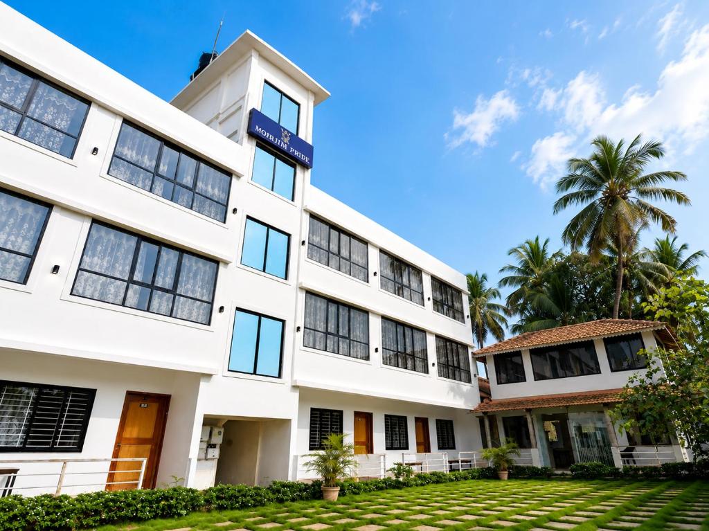 a white building with palm trees in the background at Morjim Pride Hotel with Swimming Pool near Morjim Beach in Morjim