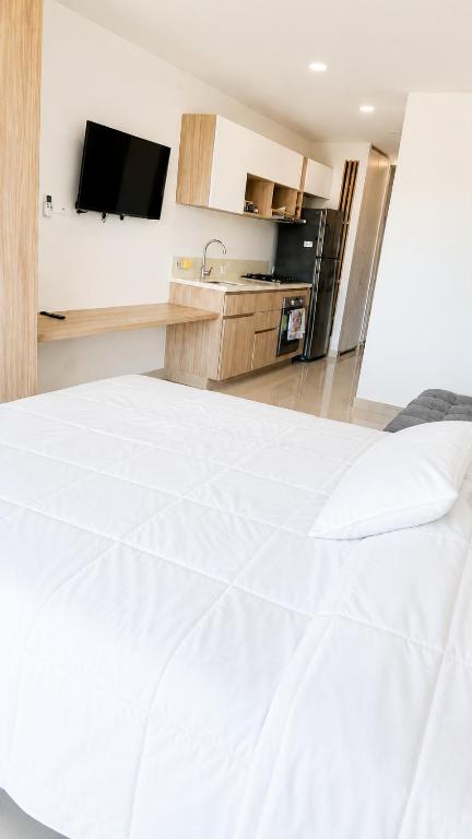 a bedroom with a white bed and a kitchen at Reserva del Mar II, Aparta suite cerca de la playa in Gaira