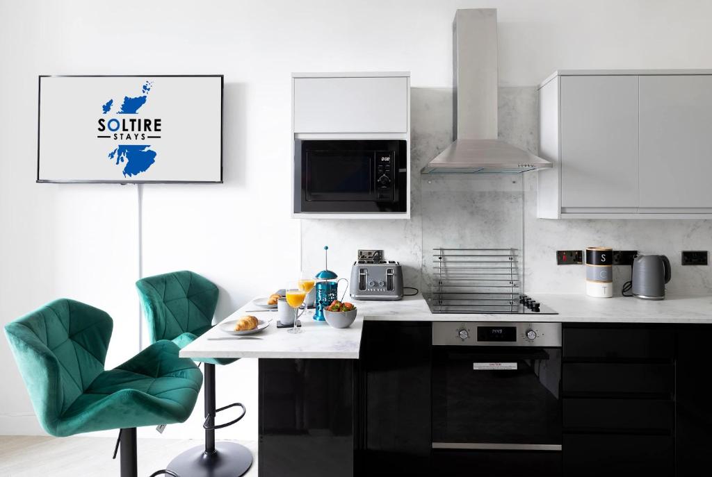 a kitchen with a white counter and green chairs at The Fountain View Apartment in Rothesay