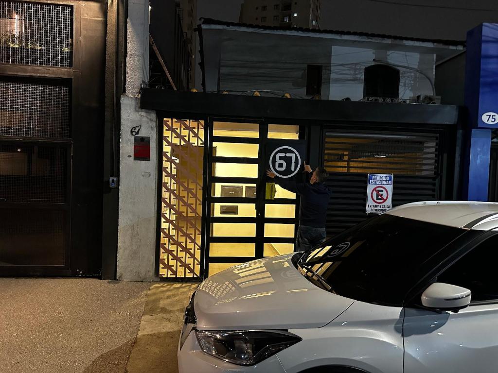 a man standing in front of a car in front of a garage at Quartos individuais vila olimpia in São Paulo