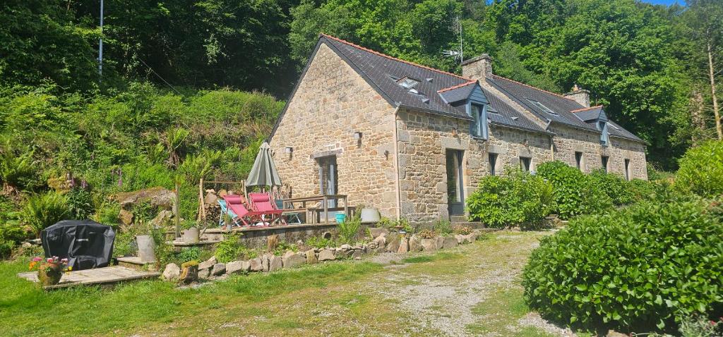 a stone house with two chairs and a umbrella at Ker Adèle, longère cosy au cœur d'un bois in Ploërdut