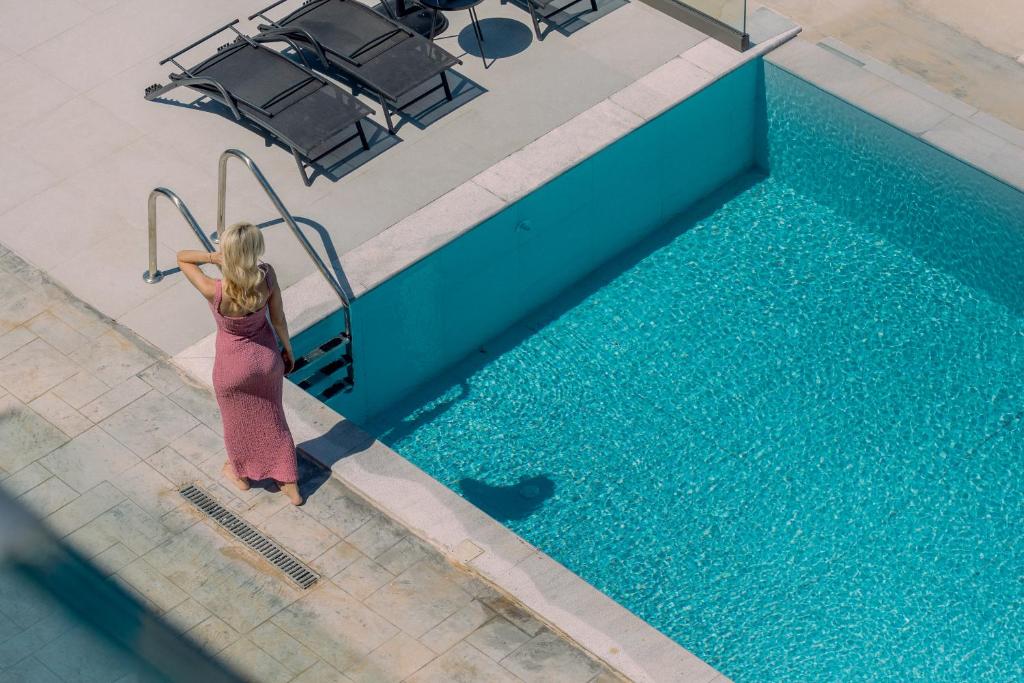 a woman in a dress standing next to a swimming pool at Pillow Apartments in Nikiana