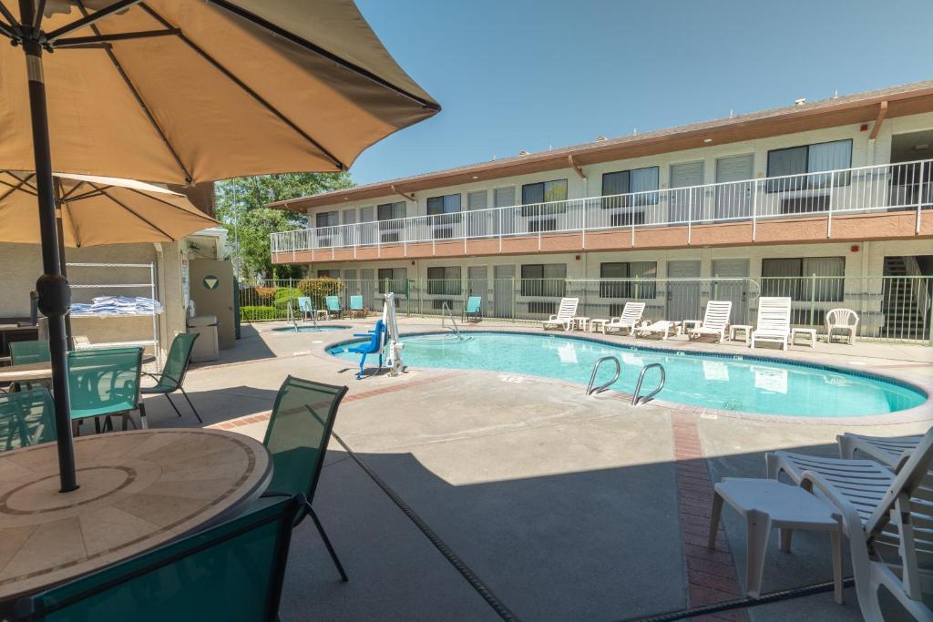 a pool with a table and chairs and an umbrella at The Oakhurst Inn at Yosemite in Oakhurst