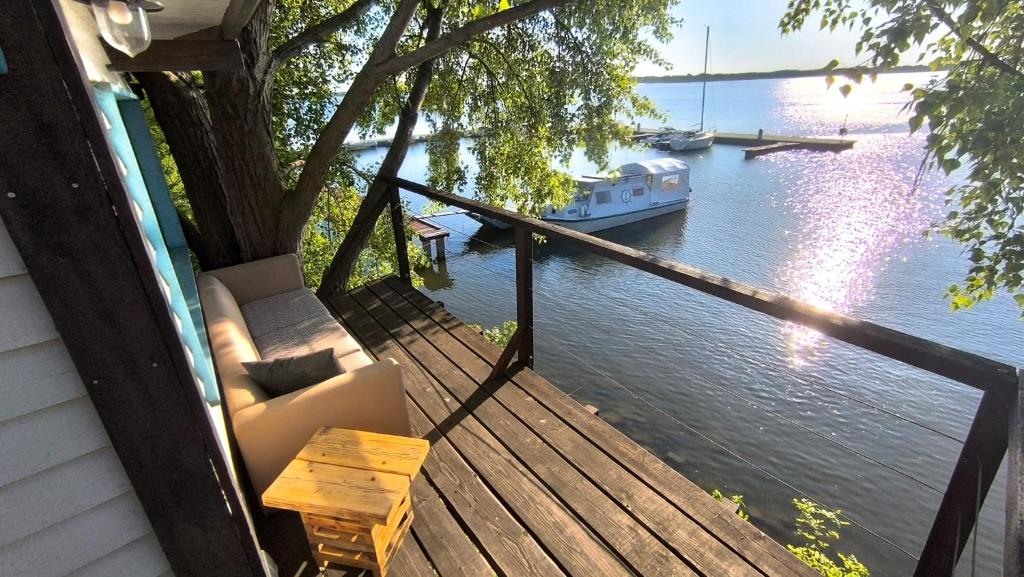 a porch with a couch and a table and a boat on the water at The Marina Treehouse in Hamuliakovo