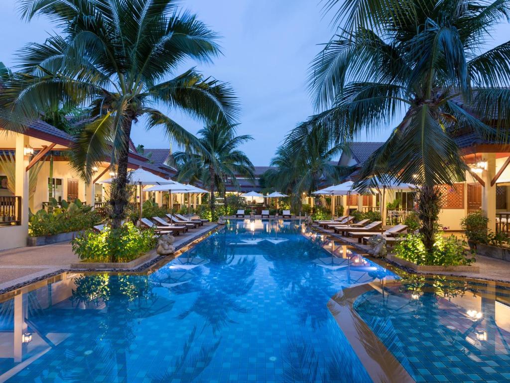 a pool with chairs and palm trees at night at Le Piman Resort in Rawai Beach