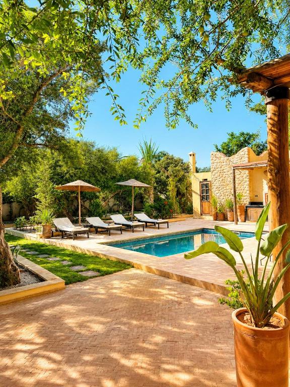 a swimming pool with benches and umbrellas in a yard at Maison Zina in Al Ghar